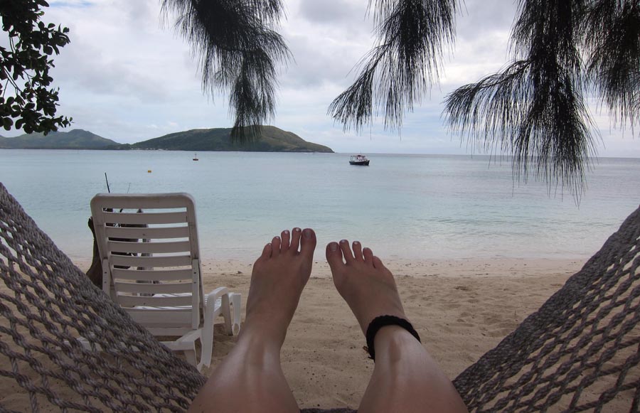 Feet of person on hammock with sea and beach in front