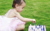 Baby playing chess with teddy on lawn