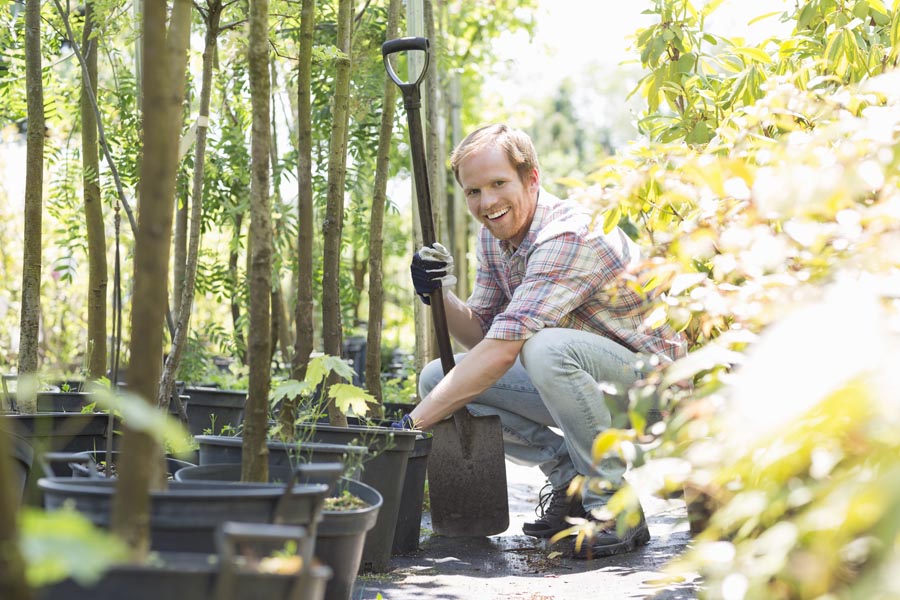 Portrait of happy gardener crouching while holding shovel at plant nursery