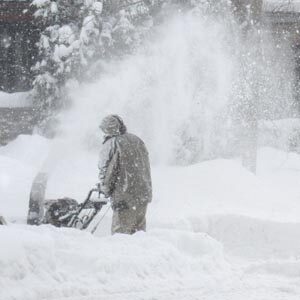 Man pushing snow blower in heavy snow storm